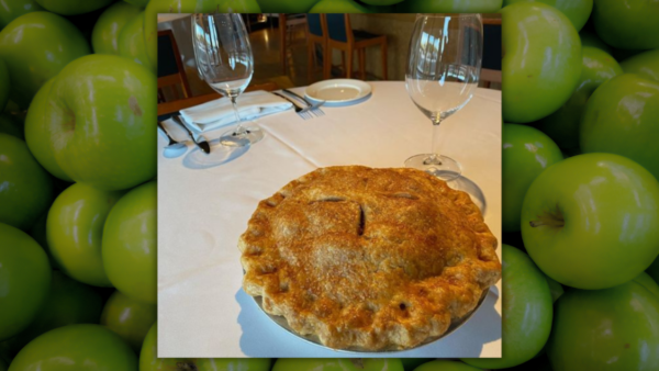 A pie sits on a white tablecloth, the table set for dessert. Courtesy Tarbell's. Background: a pile of Granny Smith apples.
