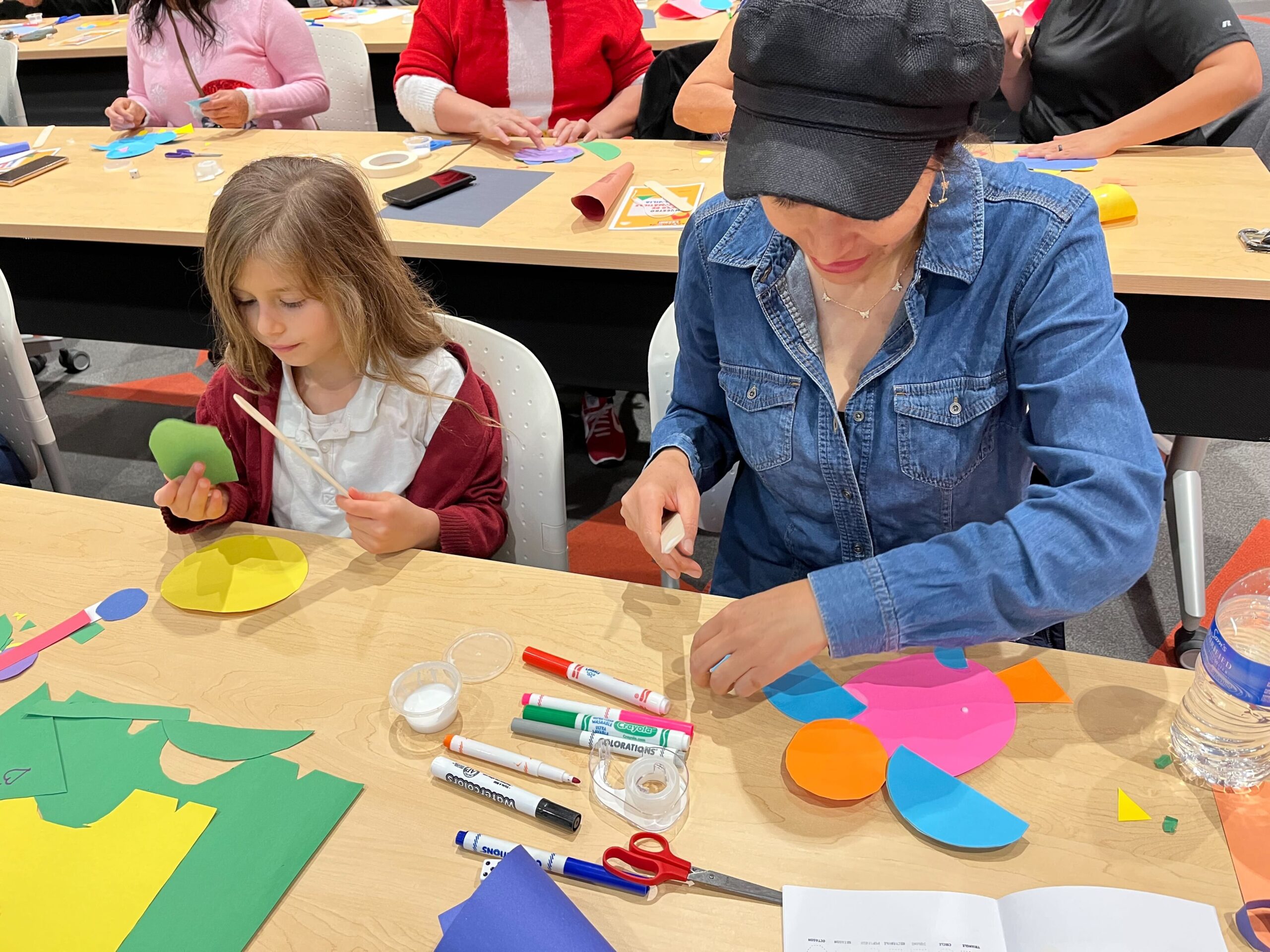 A mom and her daughter sit at a table at an AZPBS event and make crafts