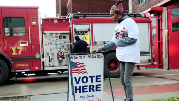 A volunteer puts up a sign with an American Flag on it that reads: Vote