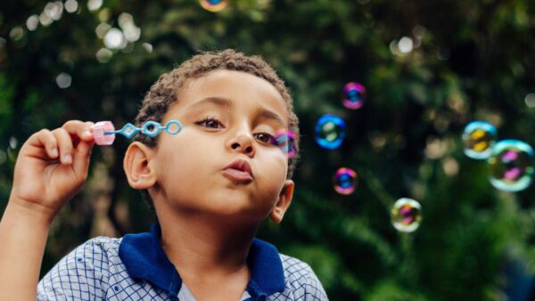 A young boy blows bubbles outside