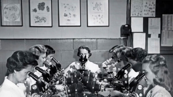 A black and white image of a group of women looking through a microscope