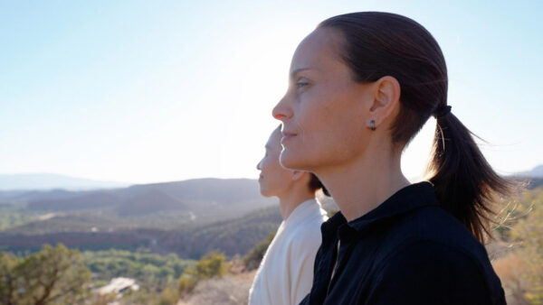 Two women stand on a cliff overlooking a scenic vista