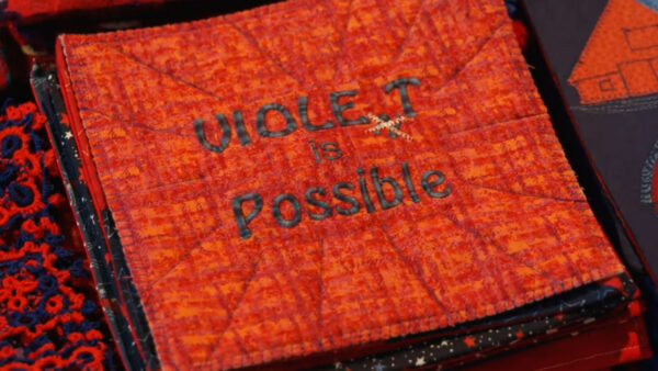 A textile with words sewn into it reading: Violet is possible