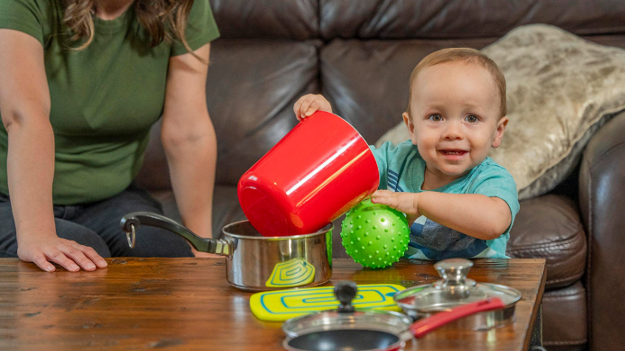 A toddler plays with a ball and a bucket on top of a table