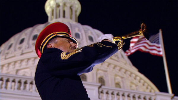 An armed forces bugler playing the trumpet in front of the United States Capitol building.
