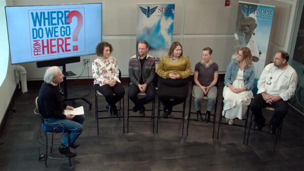 A panel discussion titled 'Where Do We Go From Here?' features six people seated in a row.