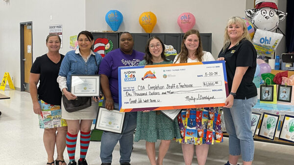 A diverse group of individuals smiling and holding a large check made out to a school.