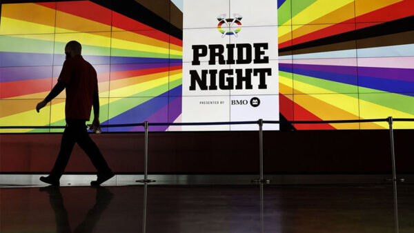 A man walks past a large screen displaying Pride Night, celebrating diversity and inclusivity.