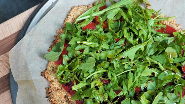 A pizza topped with arugula on a wooden cutting board.