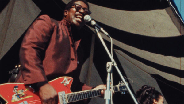 A man in a suit passionately plays guitar and sings, showcasing his musical talent in a formal setting.