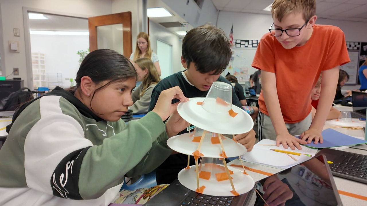 Three students working on a paper plate tower in their classroom