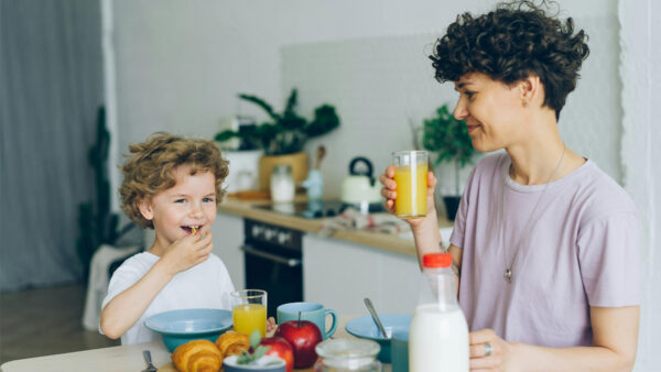 A parent sits with their young child at a dining room table