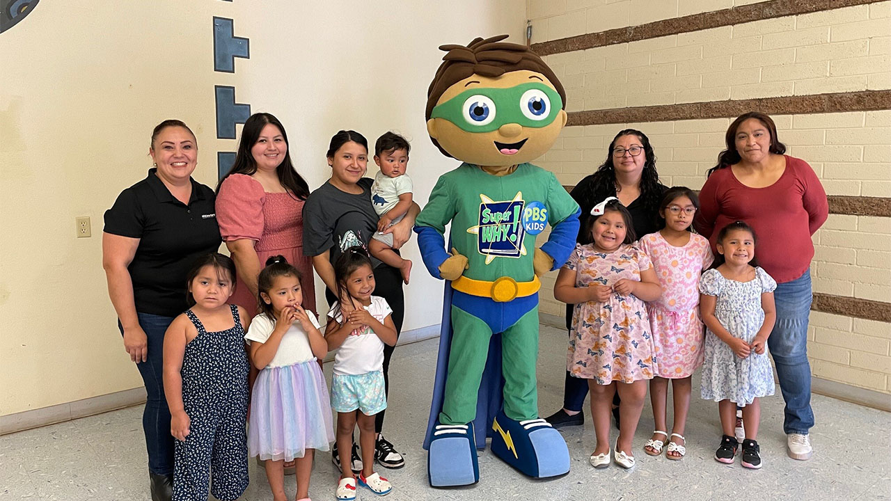 A group of children joyfully posing with a vibrant green superhero mascot.