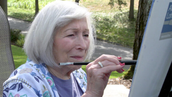 An older woman focused on painting a vibrant scene on a canvas, showcasing her artistic talent and creativity.
