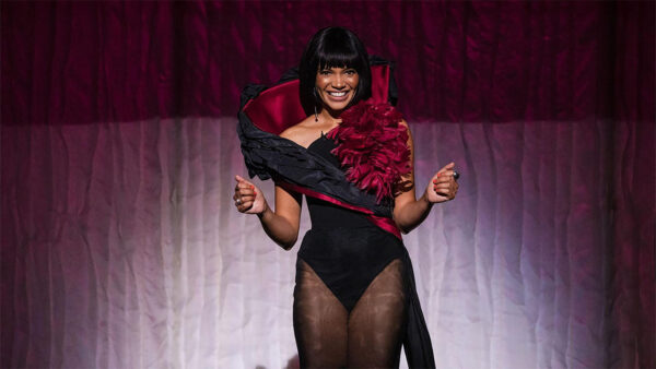 A woman elegantly dressed in a red gown, complemented by a flowing black cape, exudes confidence and style.