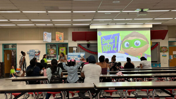 A classroom scene featuring a group of individuals seated at tables, engaged in discussion and learning activities.