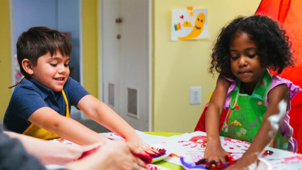 Two children joyfully painting at a table, surrounded by colorful splashes and art supplies.