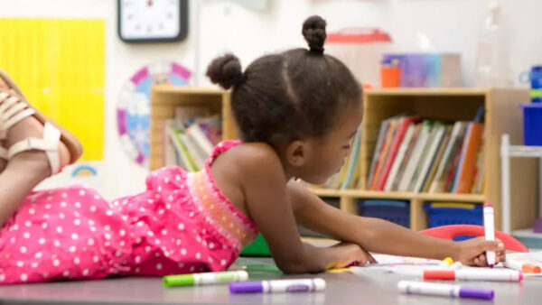 A young girl lies on the classroom floor, surrounded by colorful educational materials and a warm, inviting atmosphere.