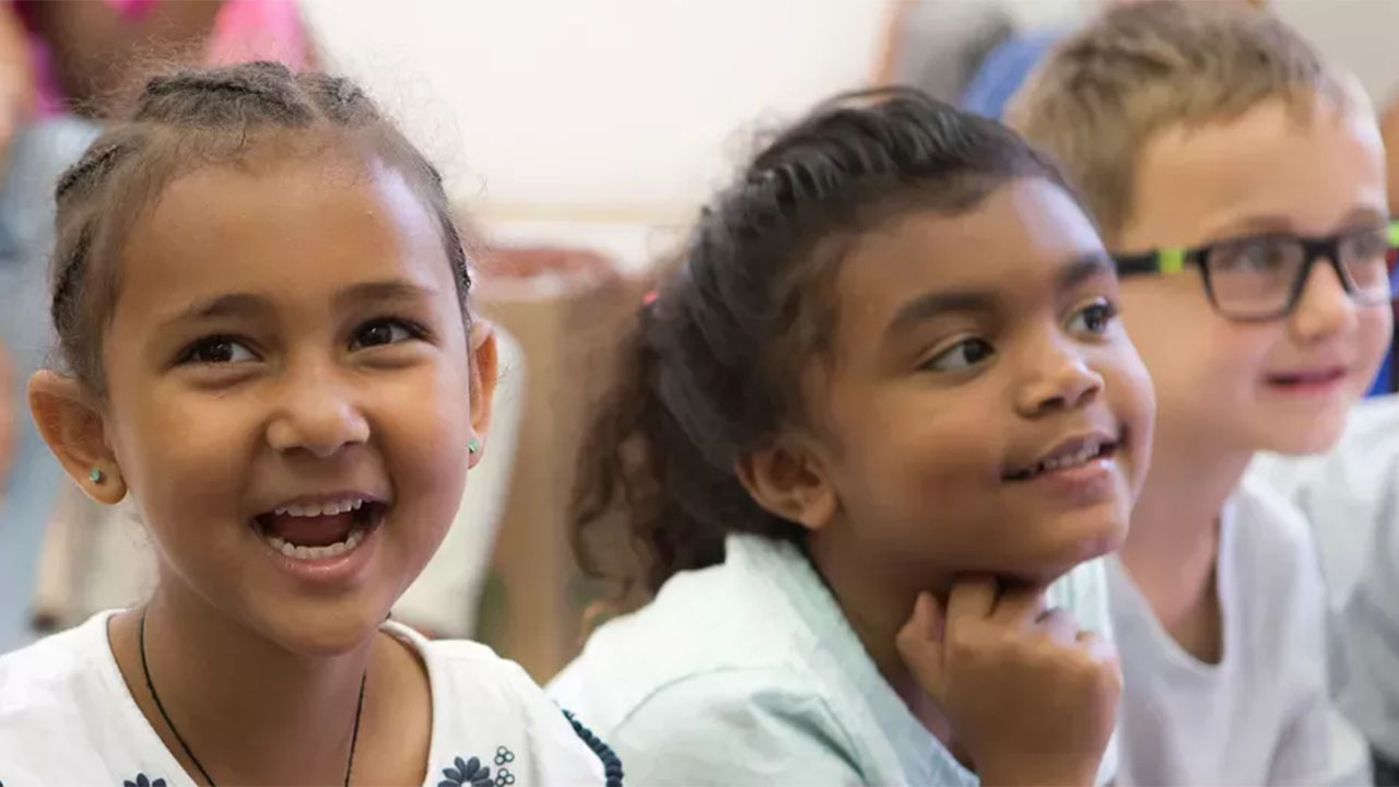 A group of smiling children seated together in a bright classroom, engaged and enjoying their learning environment.