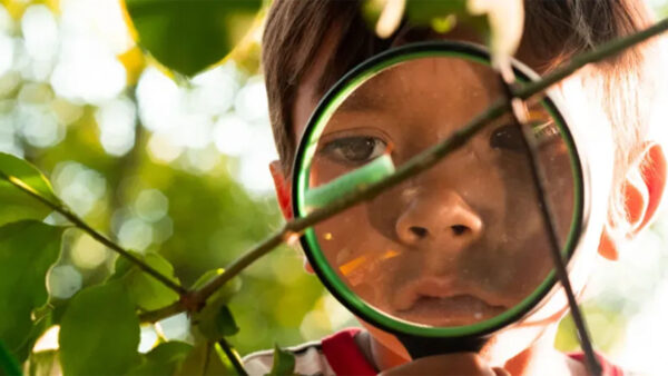 A young boy intently examines an object through a magnifying glass, showcasing curiosity and wonder.