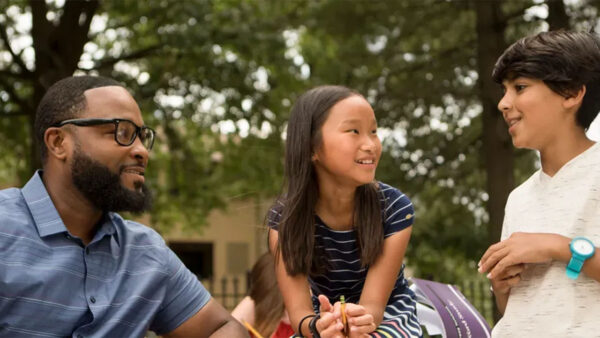 A man and two children are seated on a bench, sharing a joyful moment in a park.