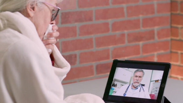 A woman in a robe sits comfortably, focused on a video playing on her laptop.