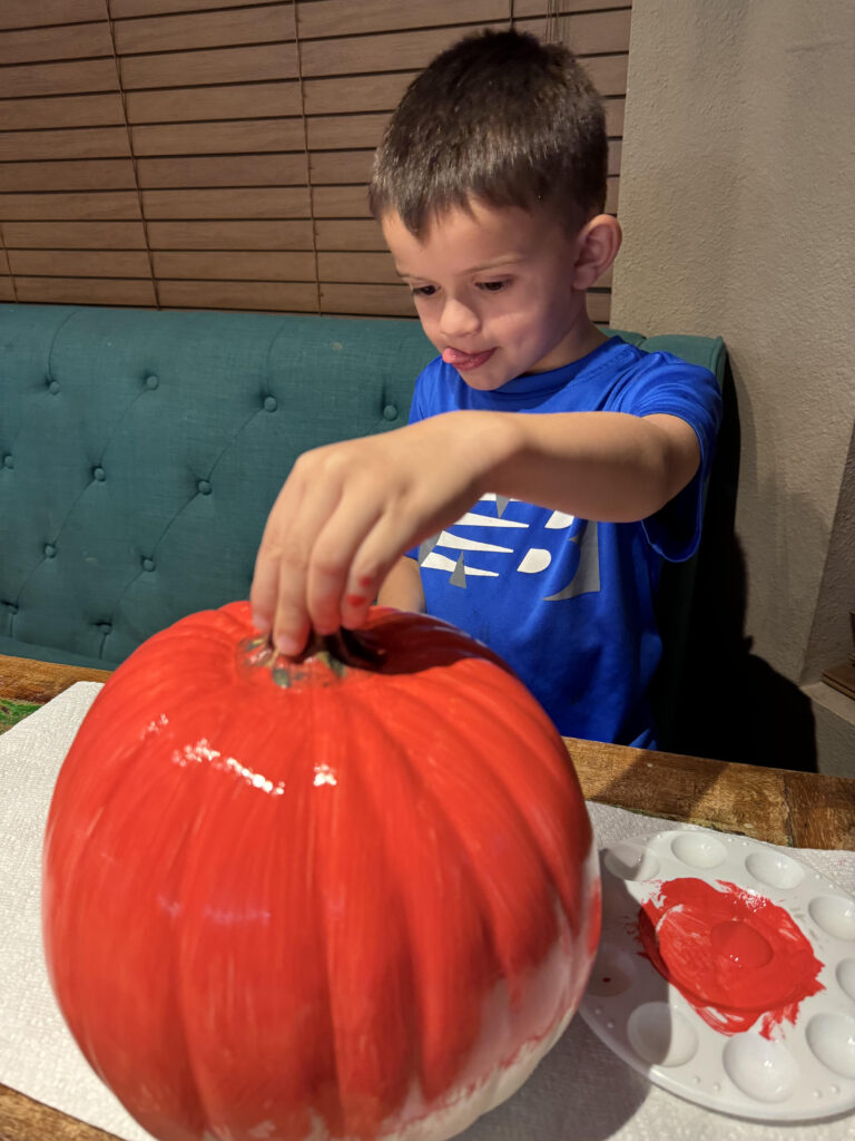 A boy painting a pumpkin red