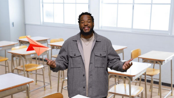 A man in a classroom smiles while holding a paper airplane, demonstrating creativity and engagement in learning.