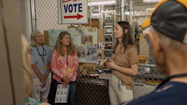 A diverse group of individuals gathered around a voting sign, engaged in discussion about the electoral process.