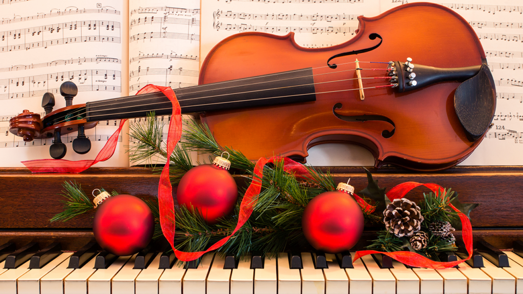 A violin sits on top of a piano with Christmas ornaments