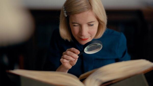 Lucy Worsley holds a magnifying glass over an old book as she reads it