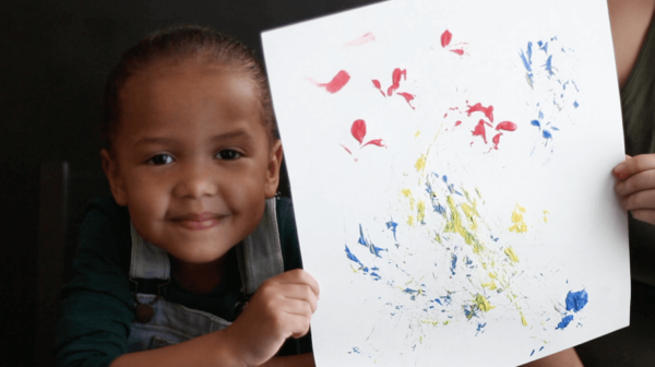 A young child creates art by painting with leaves