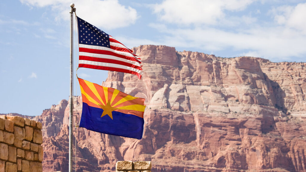 The American and Arizona flag in front of large rocks