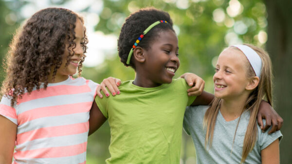 Three young girls smiling joyfully while standing closely together, showcasing their friendship and happiness.