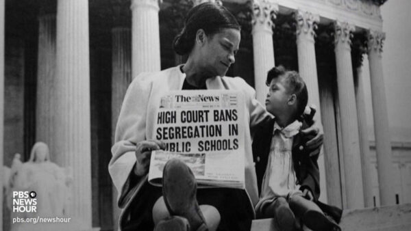 An African American woman sits next to her daughter. She holds a newspaper with the headline: High court bans segregation in public schools.