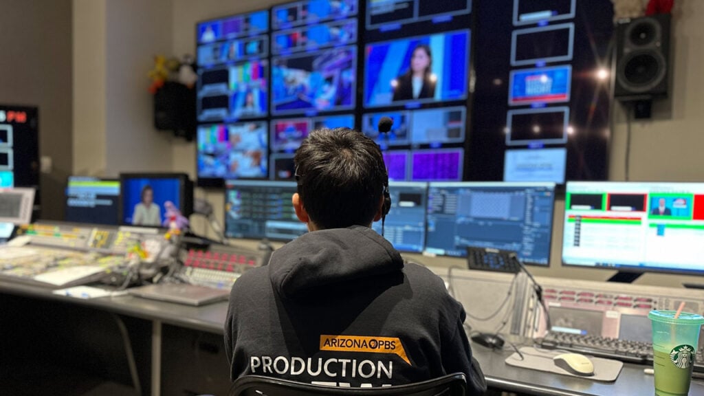A man sits in the control room wearing a hoodie with text reading: Arizona PBS Production