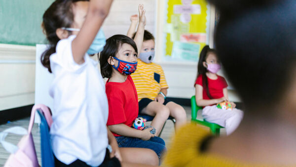 A classroom filled with children eagerly raising their hands to participate in a lesson.