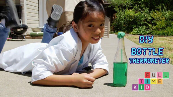 A girl lying on the ground, holding a bottle and a thermometer.