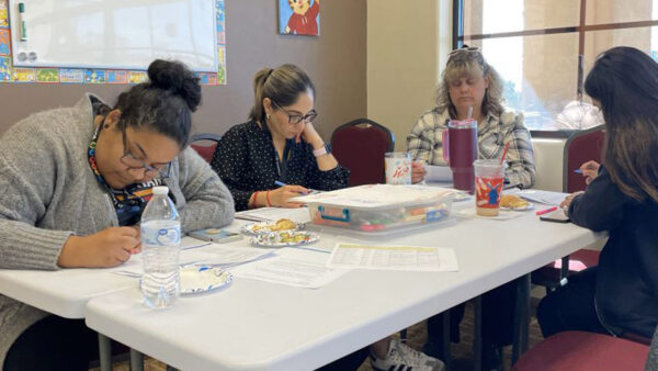 Several women gathered around a table, focused on writing and sharing ideas together.