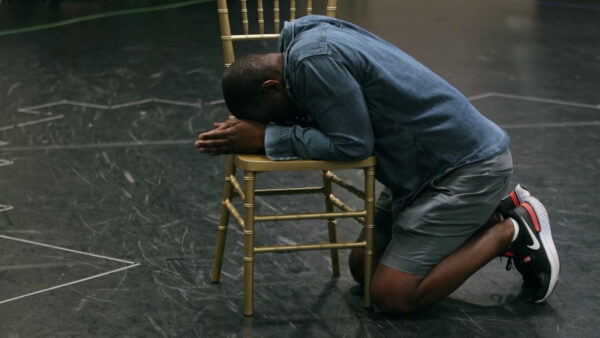 A man kneeling on the floor with his head bowed.