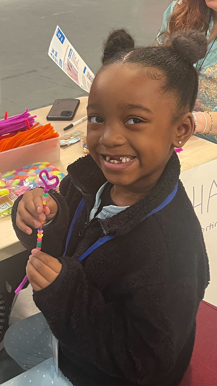 A young girl smiles brightly while holding a decorated pen