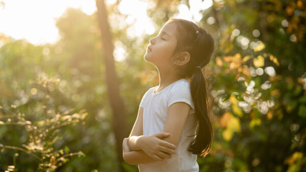 A young girl stands in a forest practicing mindfulness with her eyes closed