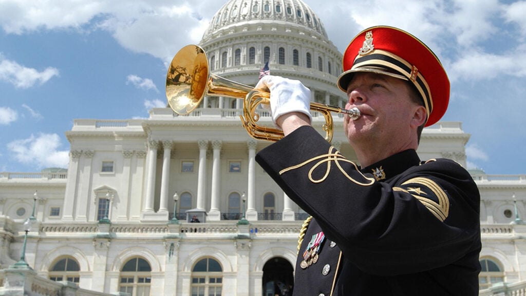 A solider playing a trumpet in front of the U.S. Capitol building