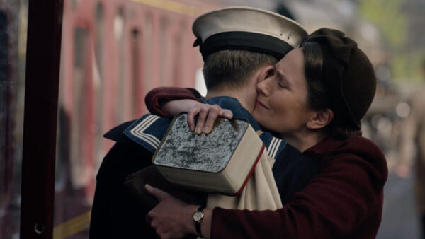 A man and woman embrace affectionately in front of a train