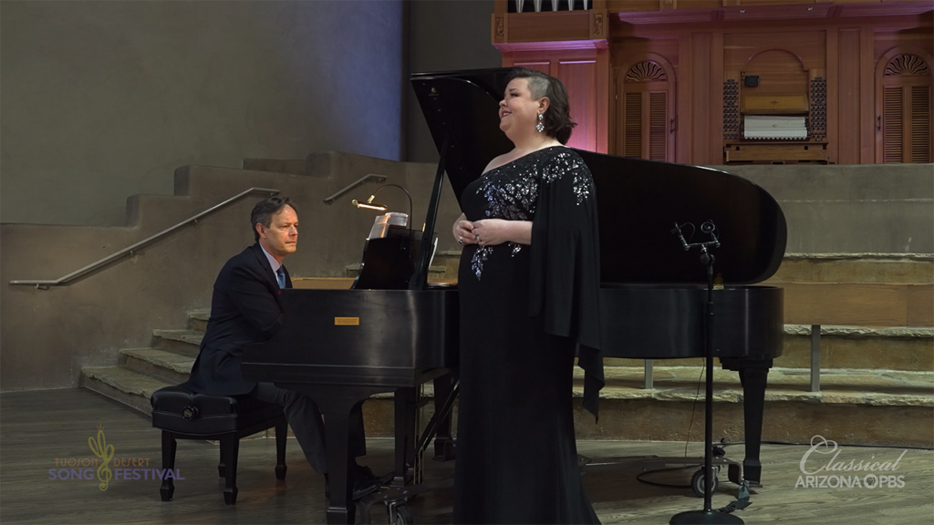 A woman sings while standing next to a grand piano as part of the Tucson Desert Song Festival