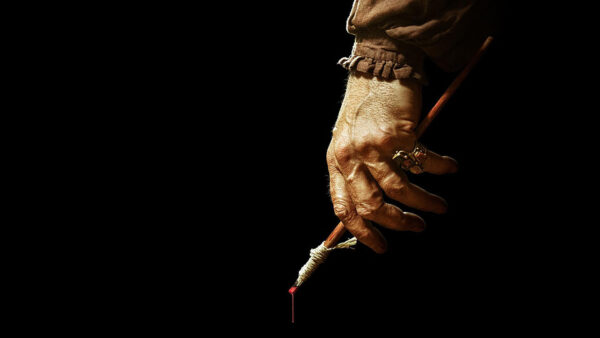A painter holding a dripping paint brush in front of a black background