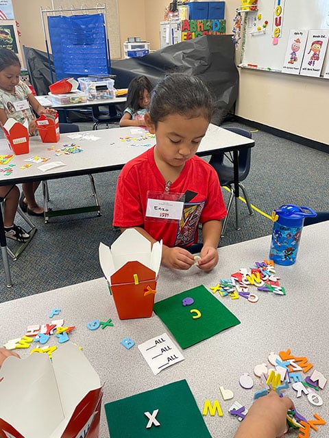 A young girl is engaged in crafting, arranging colorful letters on a table