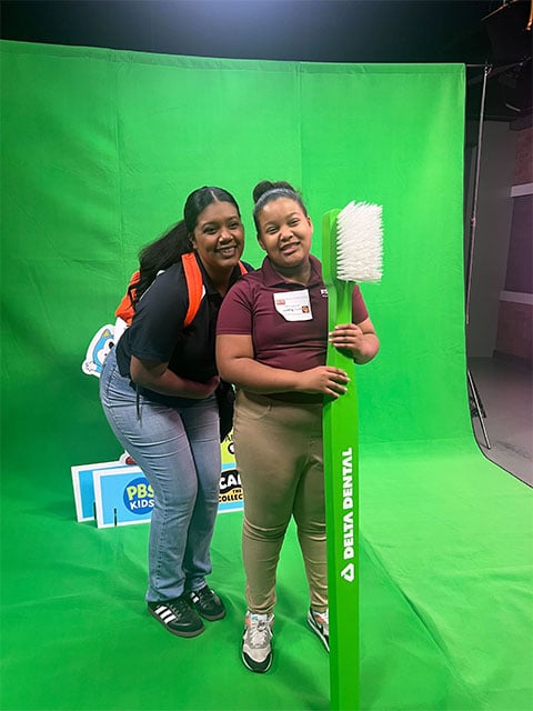 Two individuals smiling for a photo in front of a huge tooth brush