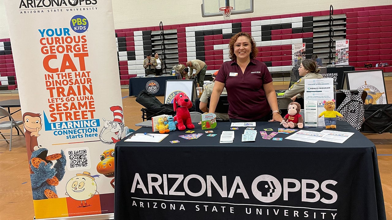 A woman stands behind a tabling of Arizona PBS