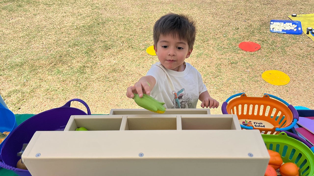 A young boy joyfully explores a colorful tray filled with various fruits and vegetables.